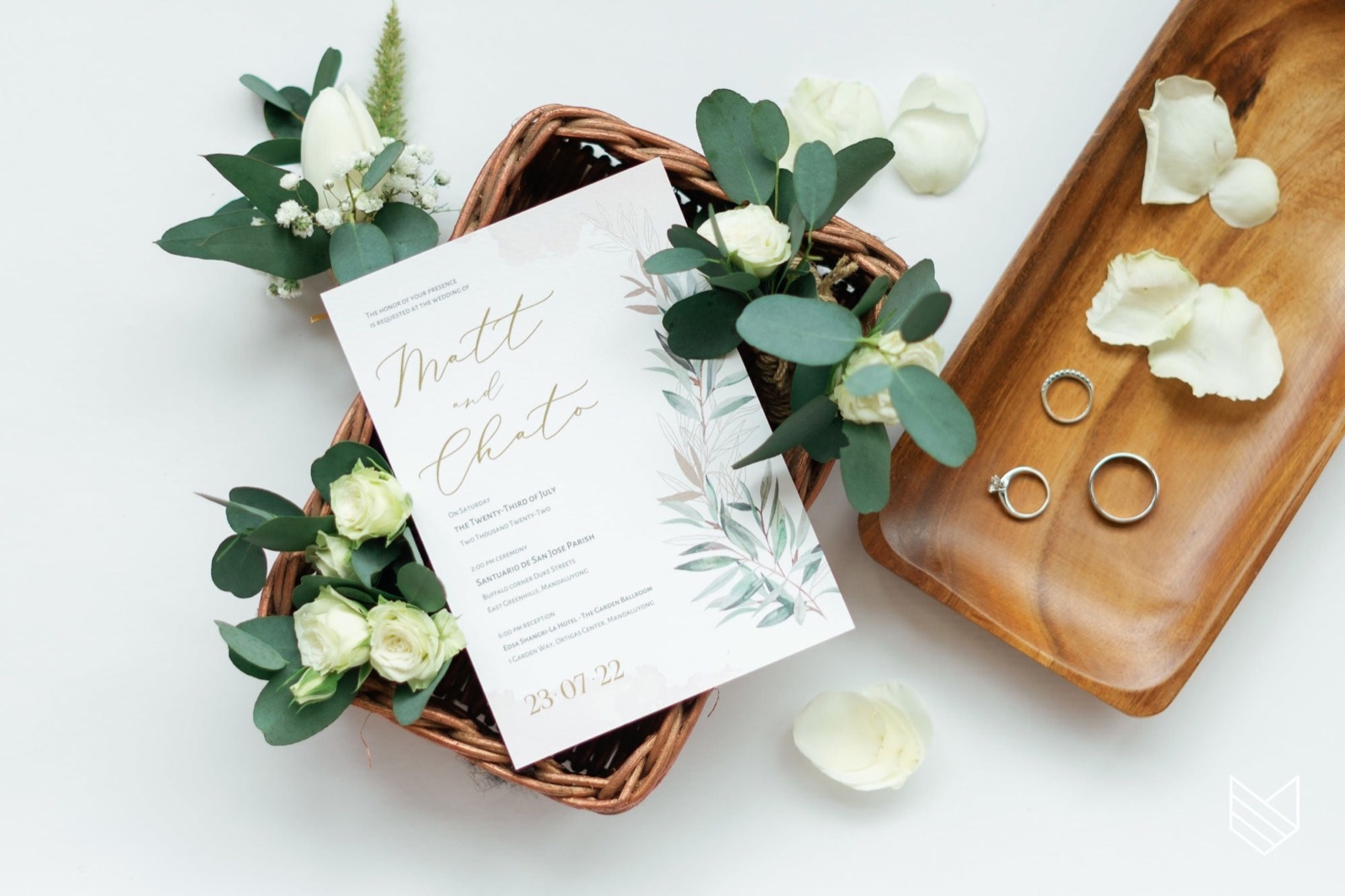 A wedding invitation suite styled with eucalyptus, white roses and wedding rings.
